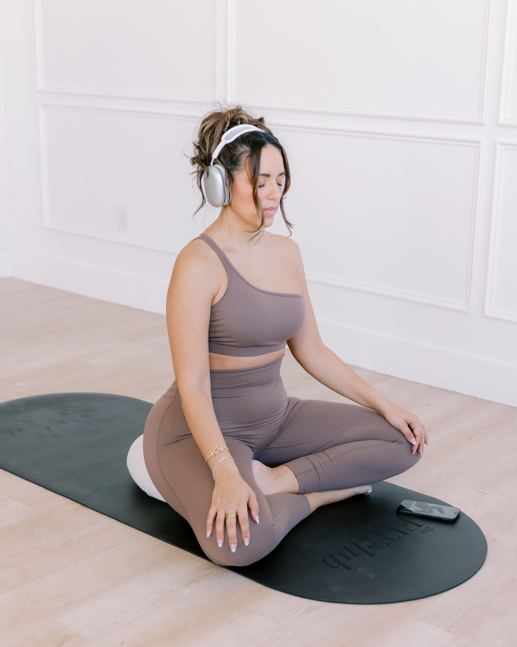 Woman sitting on a yoga mat following a meditation on her phone through The FITclub app.